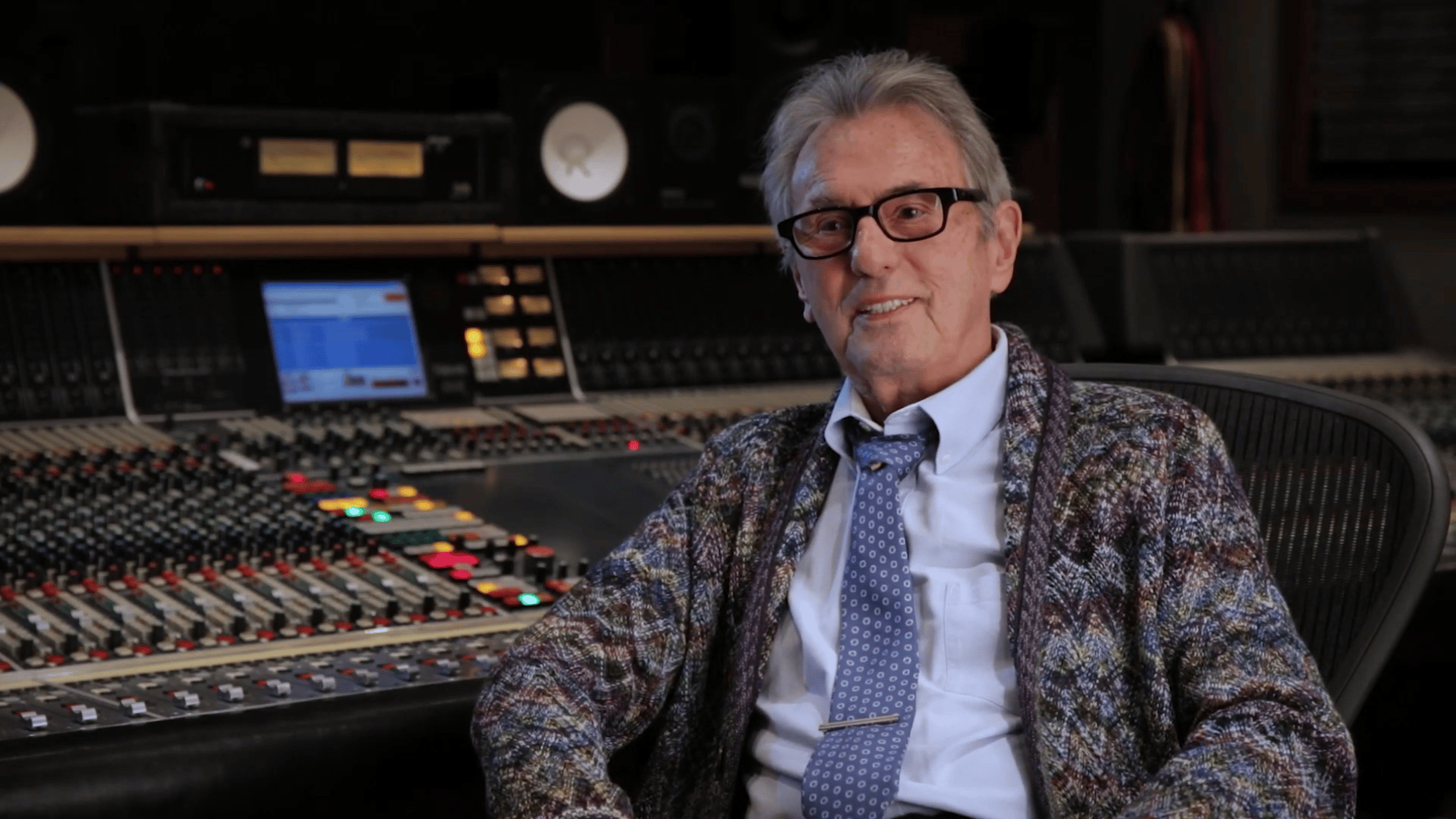 Man sitting in front of a professional audio mixing console in a recording studio.
